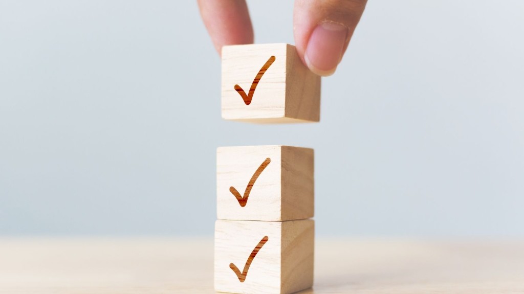 Cubos de madera con tilde superpuestos; mano colocando el último cubo como checklist cumplido.